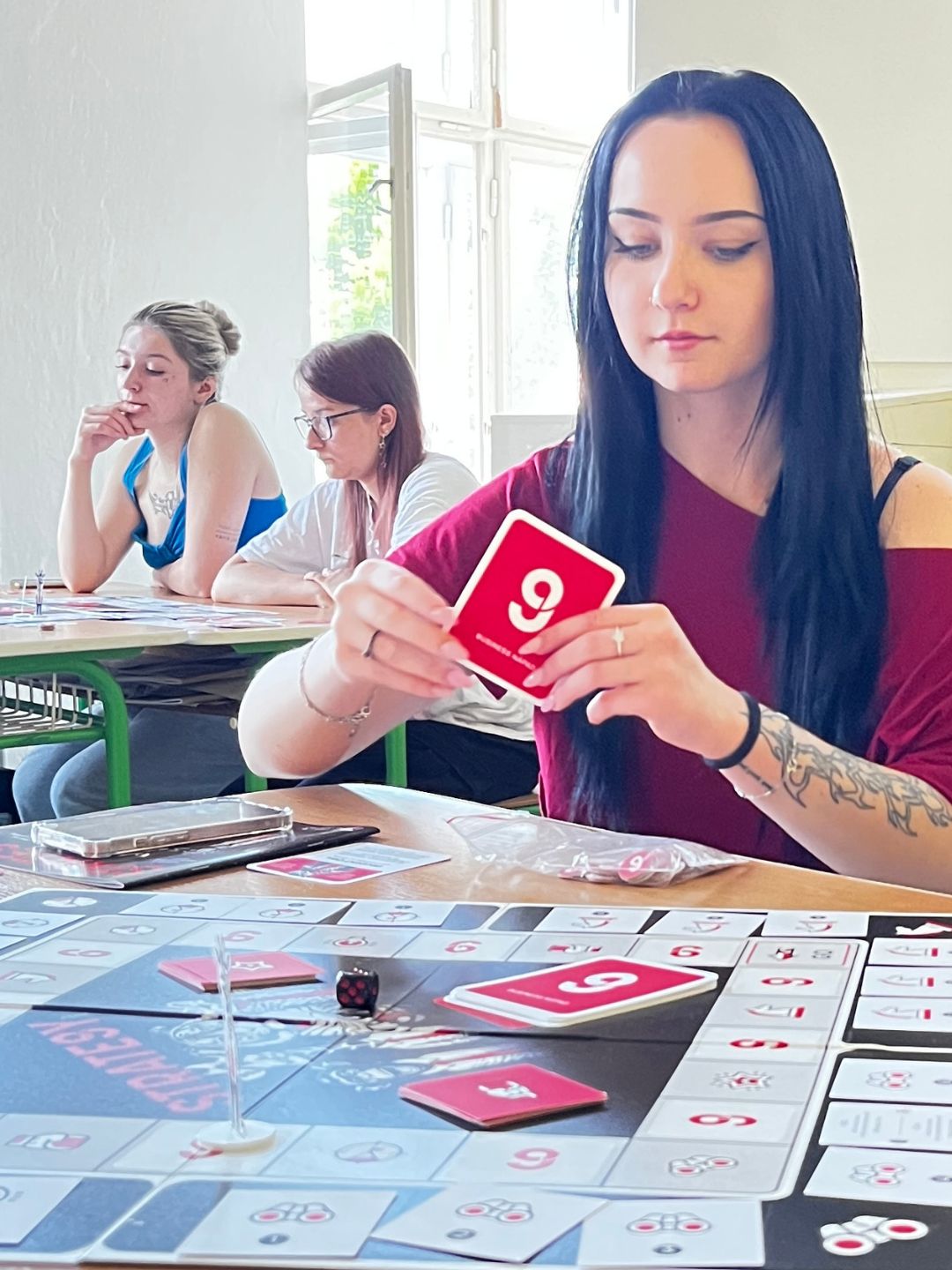 Studentka drží kartu STRATE9Y během hry